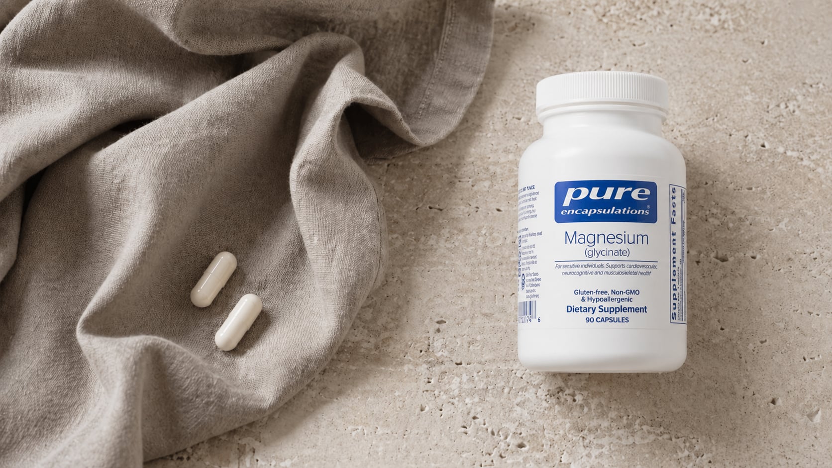 Pure Encapsulations Magnesium glycinate white bottle on a warm beige stone surface beside a draped greige linen scarf with two white capsules resting on the fabric