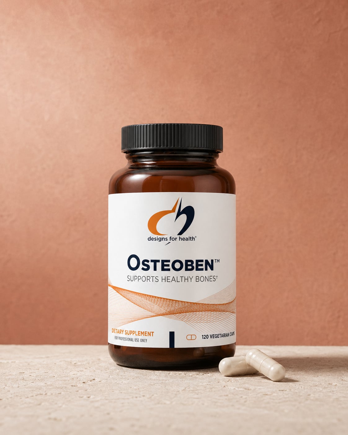 Designs for Health Osteoben amber bottle on a warm beige stone surface against a terracotta wall, with two white capsules resting at the base